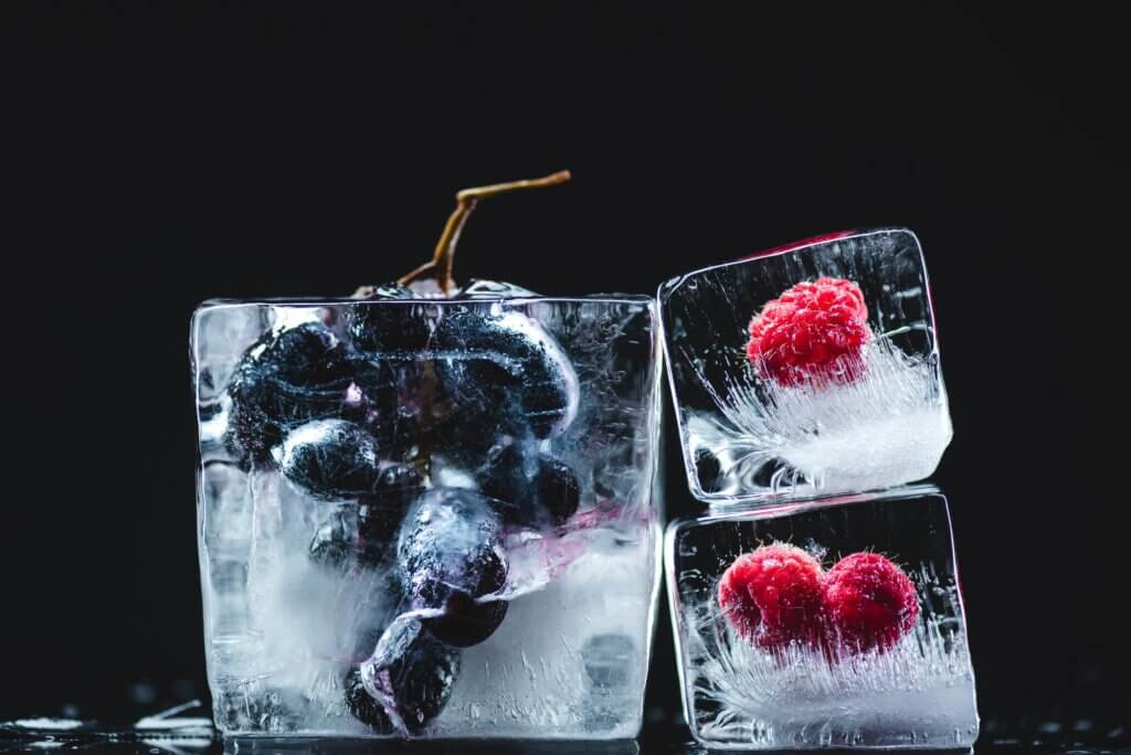 close-up view of frozen juicy grapes and ripe raspberries in ice crystals on black